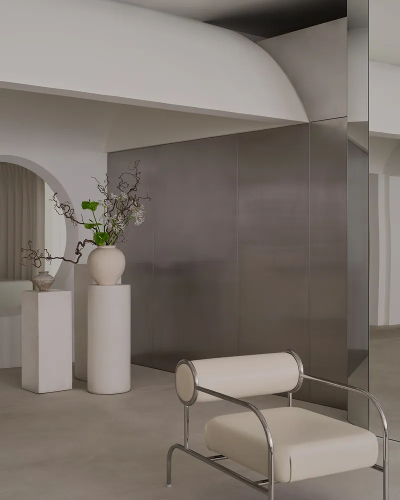 Close-up of cream upholstered chair with cylindrical armrests beside grey metal wall panels and white pedestals