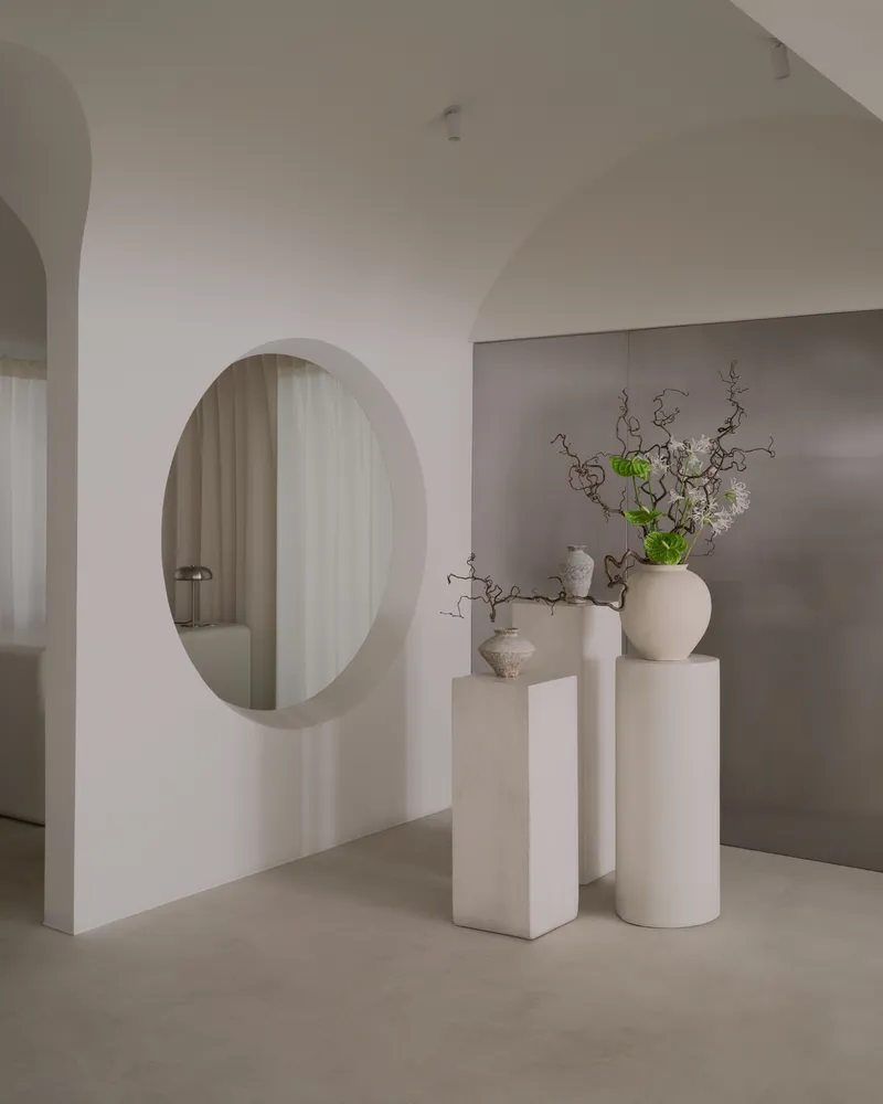 Circular aperture in white wall framing view of sheer curtains with ceramic vases on pedestals in foreground