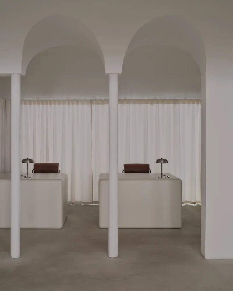 Symmetrical pair of arched alcoves with white columns, sheer curtains, and upholstered seating blocks with table lamps