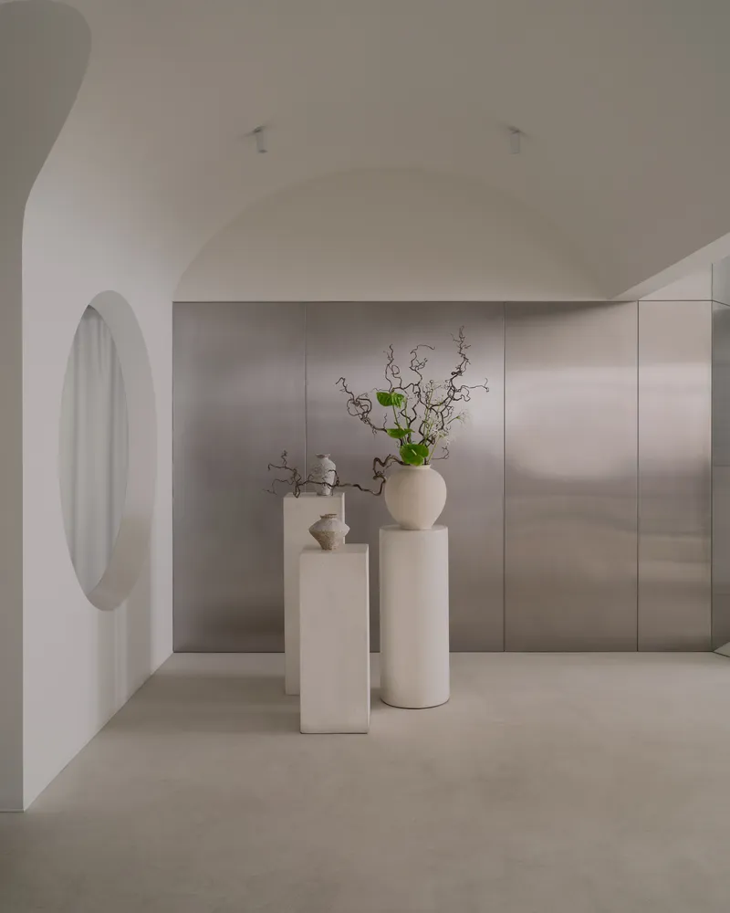 Arched hallway with circular window opening onto stone-paneled wall and ceramic pedestals with green branches