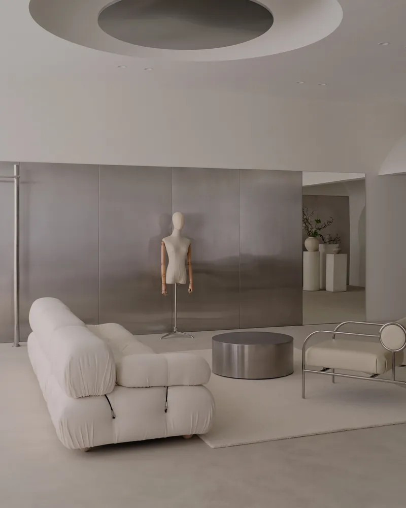 Retail interior with circular ceiling recess, dress form mannequin, and brushed metal coffee table