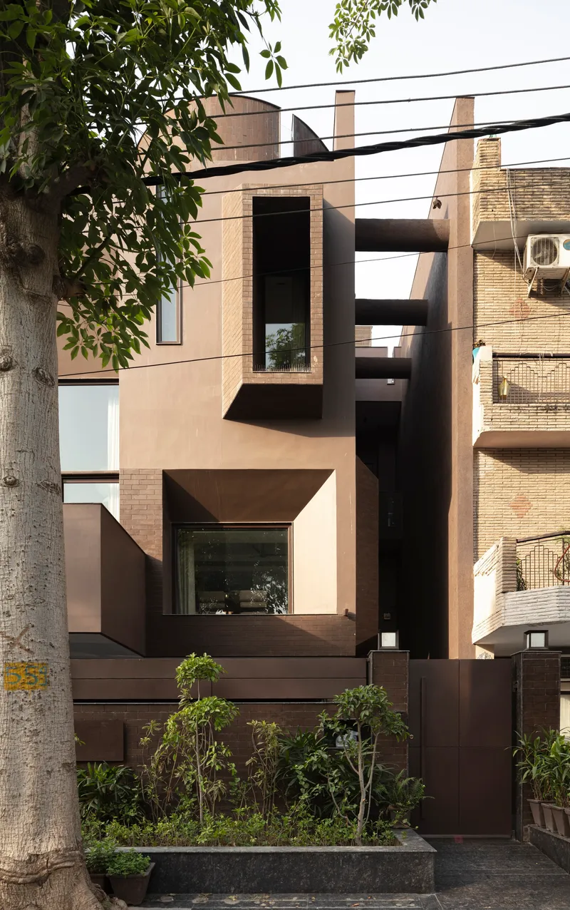 Street facade with geometric bronze-framed windows and planted bed framed by a street tree
