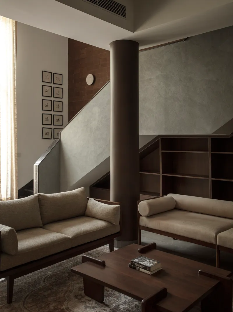 Living room with central column and framed artworks hung along the brown tiled staircase wall