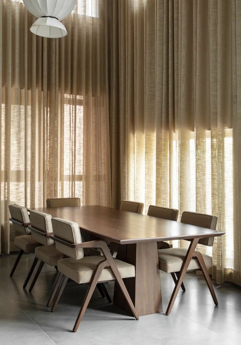 Dining area with timber table and chairs beneath layered linen curtains filtering soft daylight