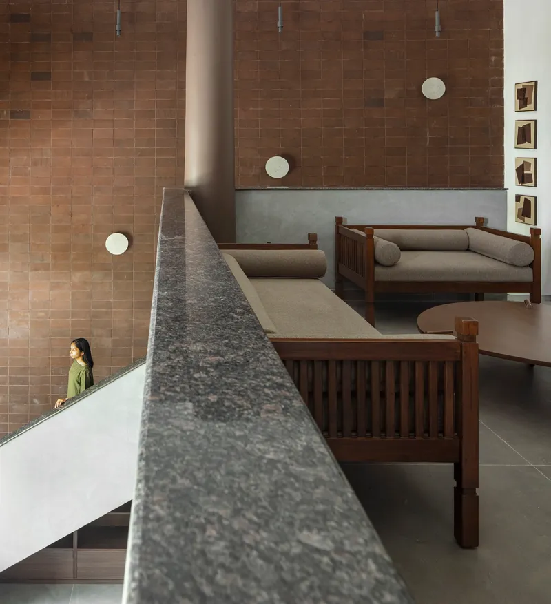 Interior view of terrazzo-clad staircase with timber furniture and figure descending along brown tiled wall