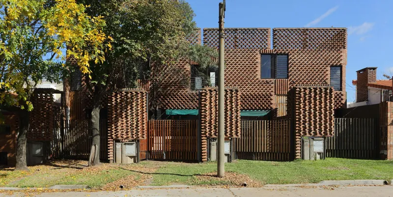 Street view of the perforated brick facade with vertical timber screens and autumn trees
