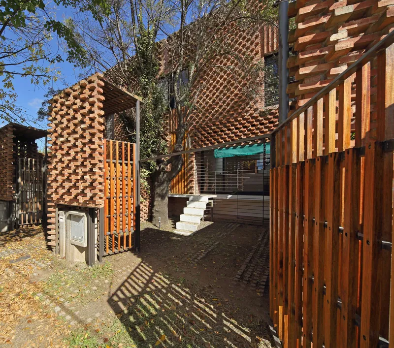Entry path through timber slat screens leading to concrete stairs beneath patterned brick walls