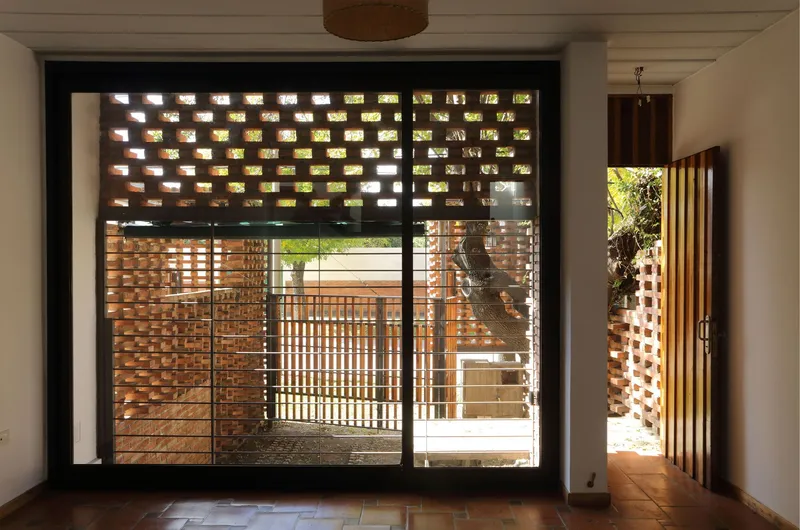 Interior view through glazed doors framing the perforated brick courtyard and timber slats beyond