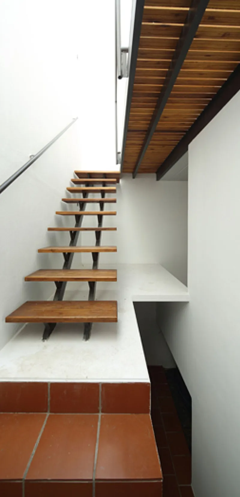 Open timber tread staircase with steel stringers ascending beneath a slatted wood soffit