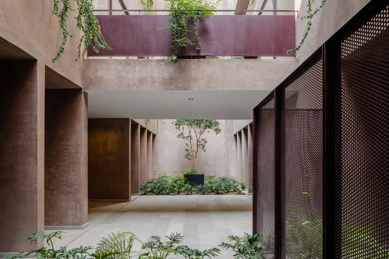 Interior courtyard with perforated metal screens, concrete columns, and cascading vines from the upper balcony