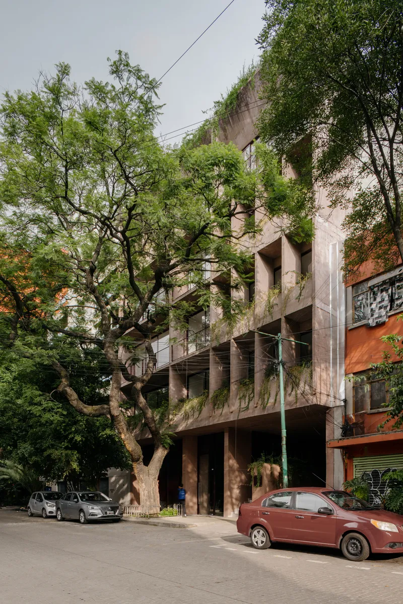 Street view showing concrete balconies with cascading greenery and adjacent tree beside parked cars