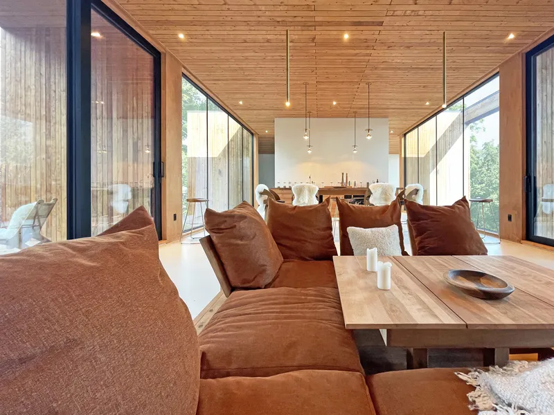 Open living area with timber plank ceiling and corner glazing overlooking the forest