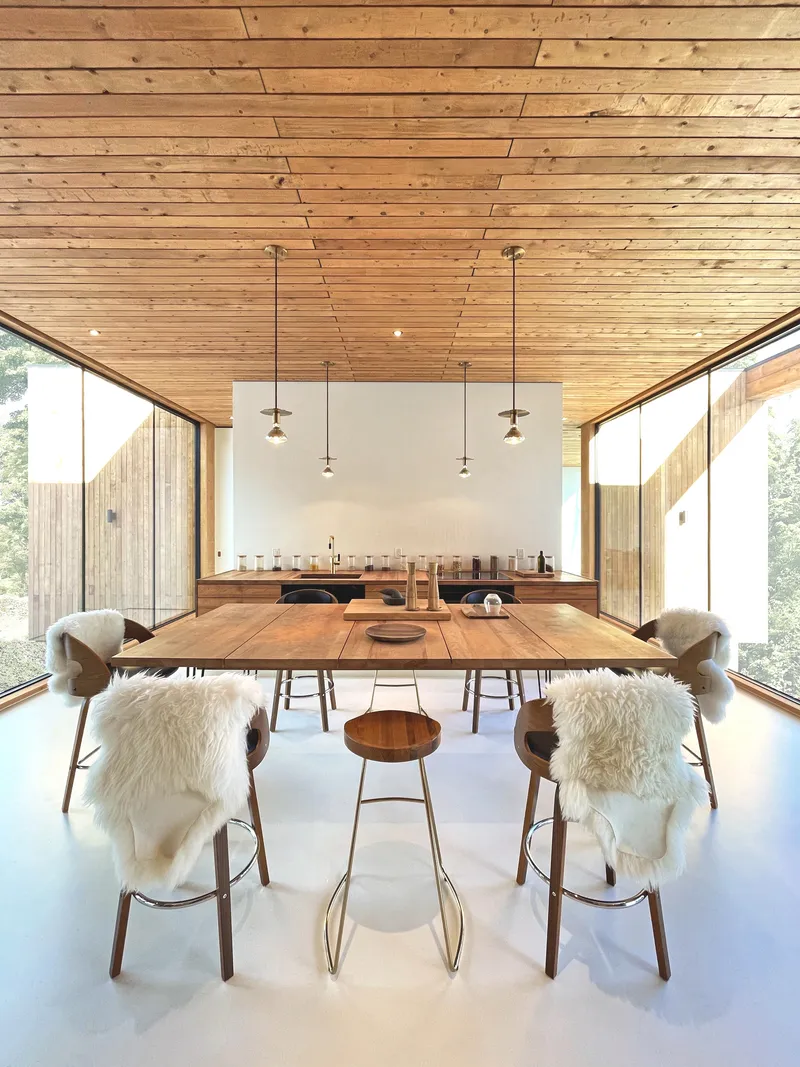 Dining room with pendant lights suspended from angled timber ceiling and glazed corners