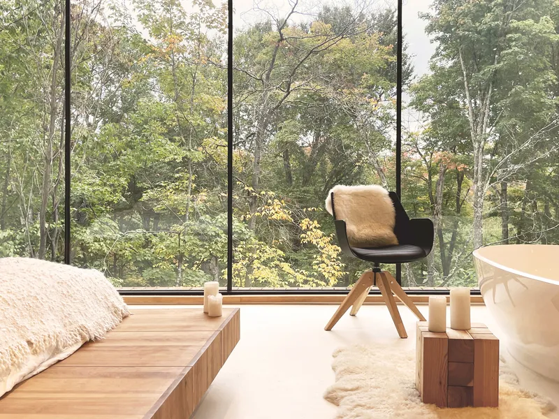 Bedroom interior with full-height windows overlooking autumn woodland and timber platform bed