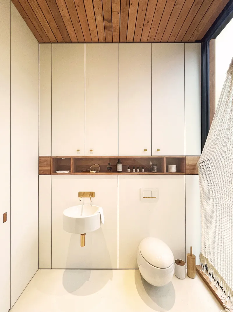 Compact bathroom with white wall-mounted sink and toilet beneath timber plank ceiling and recessed shelving