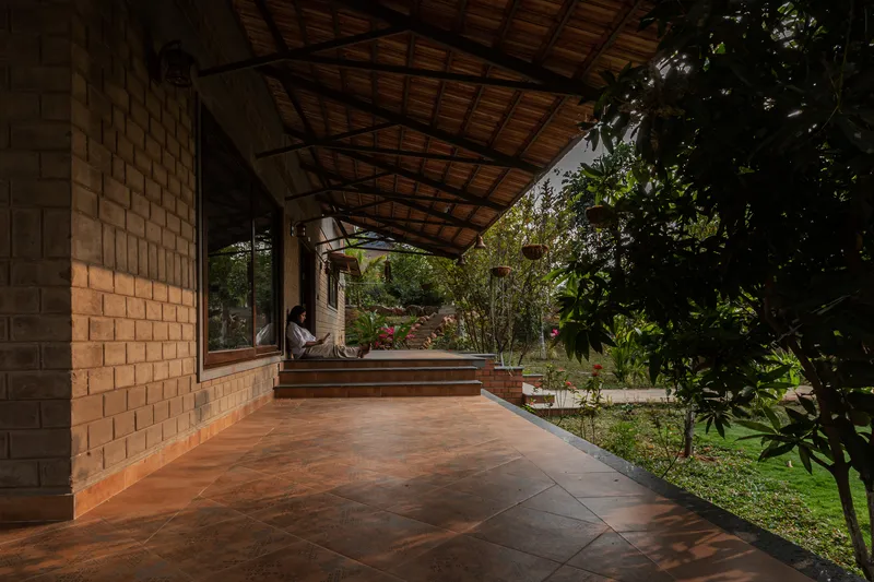 Covered terrace with exposed timber roof and terracotta tile floor opening to a garden with trees