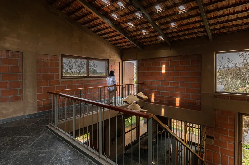 Upper-level walkway with timber ceiling beams and steel railing framing red brick walls punctured by windows