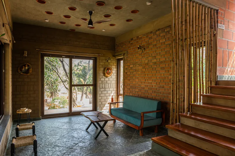 Living area with brick walls, perforated ceiling panels and timber staircase beside a vertical slat screen