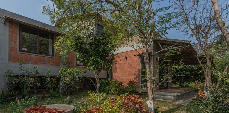 Courtyard view of the brick volumes with overhang and planted garden beds beneath mature trees