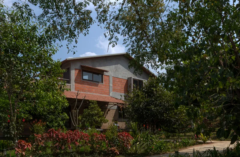 Two-storey volume with red brick upper level and curved roof seen through surrounding garden trees