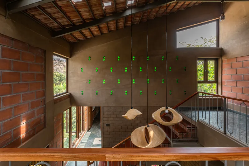 Double-height interior with timber ceiling beams, clay brick walls, pendant lights, and metal railings around a central void