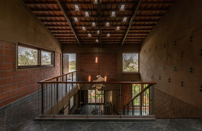 Upper-level walkway with exposed timber roof joists, steel railings, and red brick wall illuminated by afternoon light