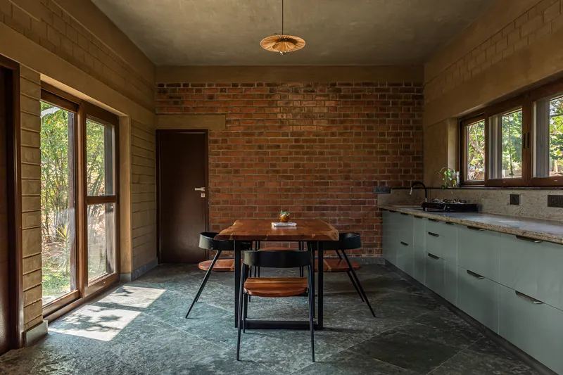 Dining area with red brick accent wall, pale green kitchen cabinets, and polished concrete floors in natural daylight
