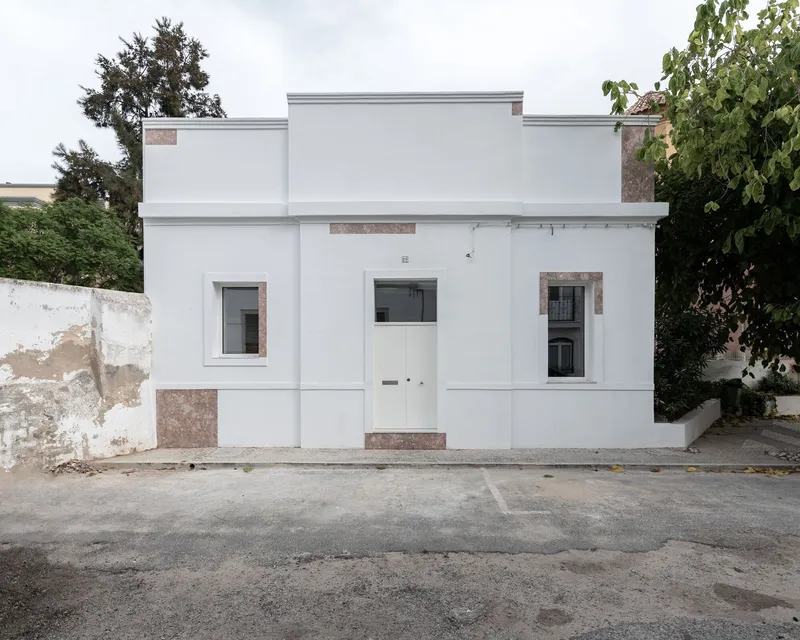 Street facade with white stucco walls and stone accents flanked by weathered perimeter walls and trees