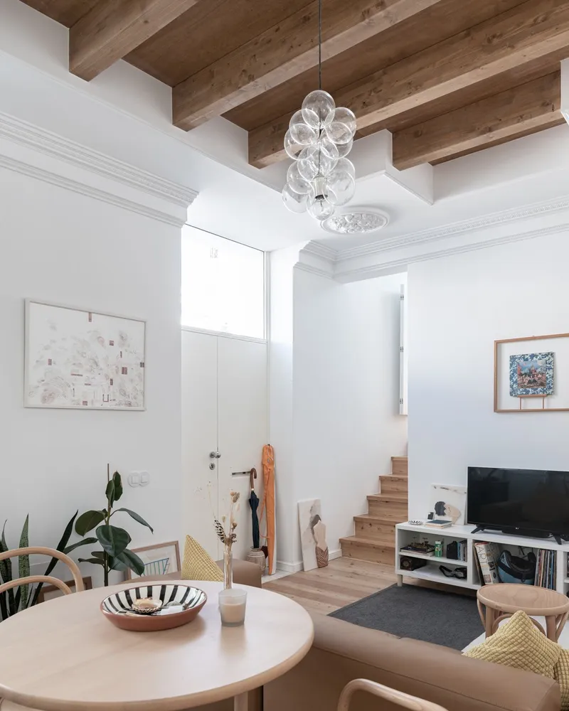 Double-height living space with exposed timber beams and a glass bubble chandelier over a dining table
