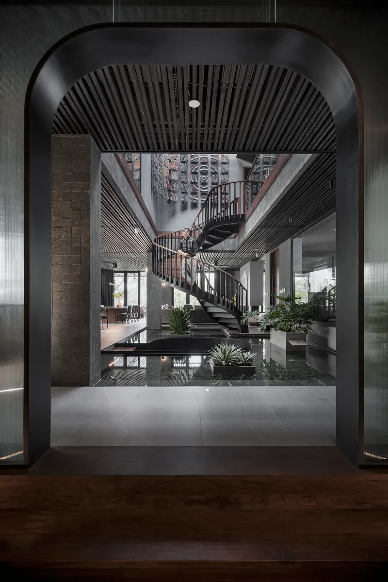 View through an arched threshold into the atrium space with spiral stair and slatted black ceiling