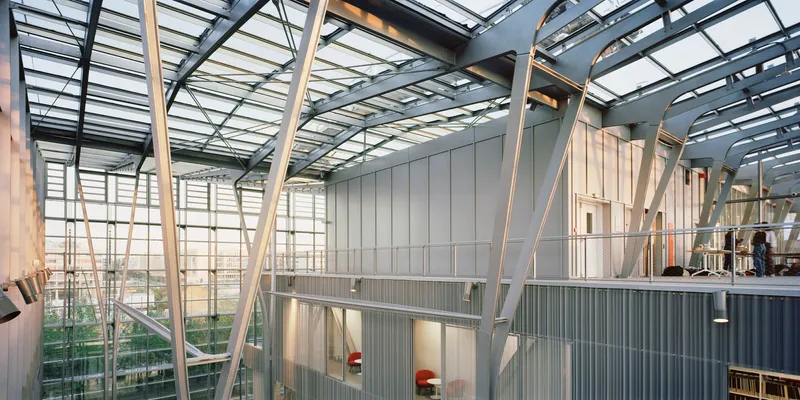 Interior view of the diagonal steel truss roof structure above corrugated metal clad volumes at dusk