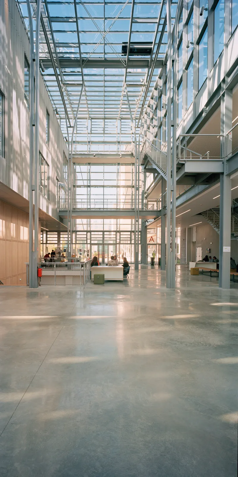 Interior atrium with glass roof structure and steel columns casting shadows on polished concrete floor