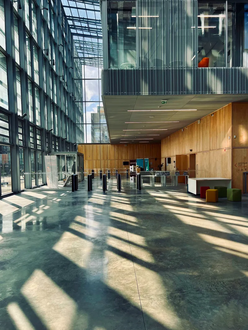 Lobby entrance with timber-clad reception desk and turnstiles beneath translucent ceiling panels filtering daylight