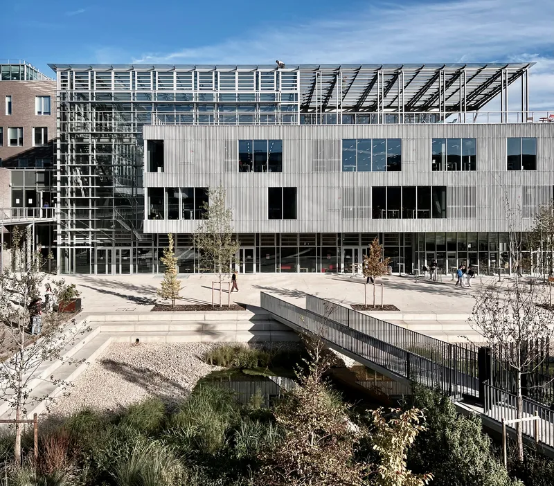 Courtyard view of the corrugated metal facade with pedestrian bridge crossing over planted beds below