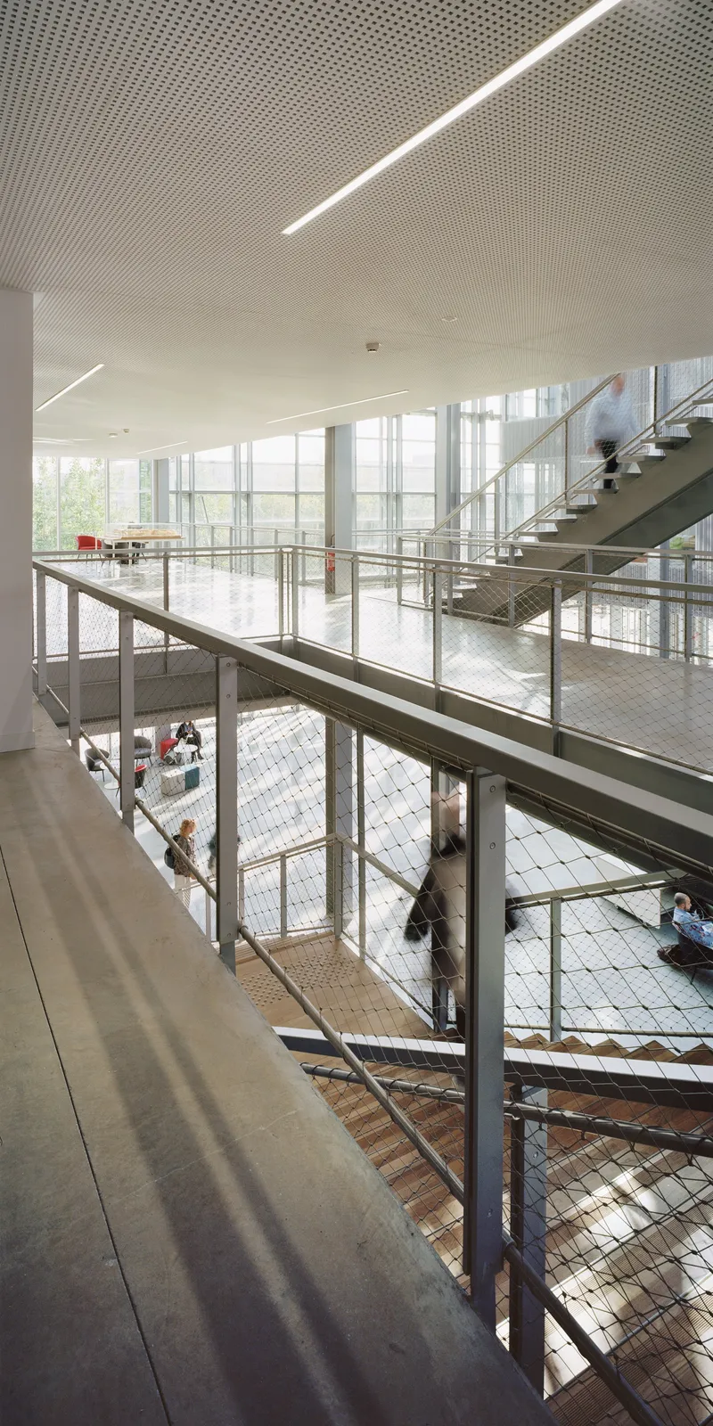 View down through metal mesh balustrades to the checkered floor with people seated on lower levels