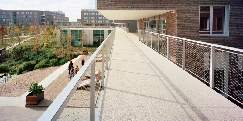 Elevated pedestrian bridge with metal mesh railings connecting brick buildings across a landscaped courtyard