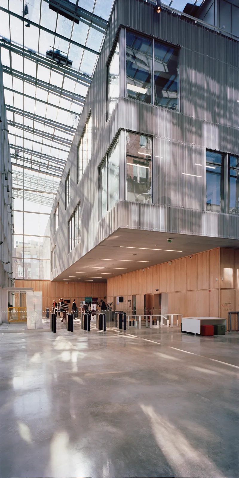 Double-height lobby with polished concrete floors and translucent corrugated facade panels above timber-clad security turnstiles