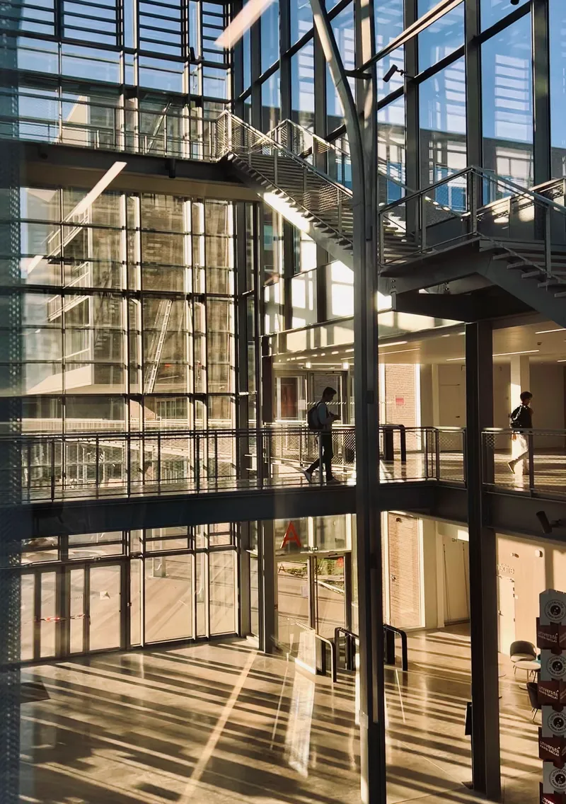 Multi-story atrium with steel bridges spanning between glass-walled floors and exposed structural columns in afternoon light