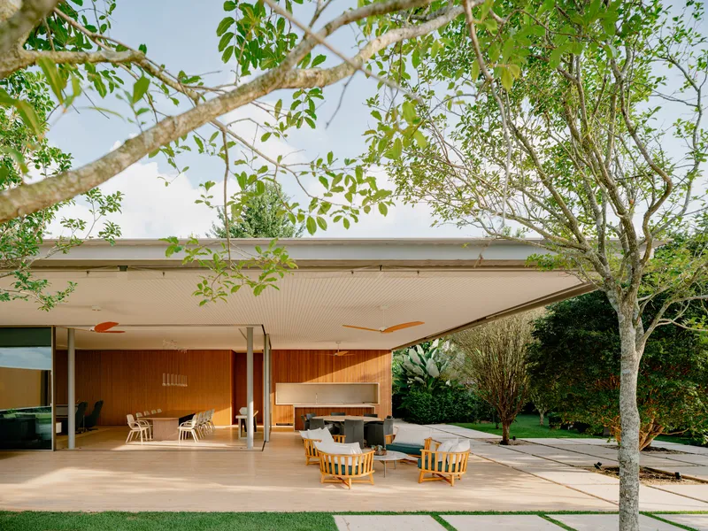 Covered terrace with white ceiling panels and timber-clad wall opening to a lawn framed by trees