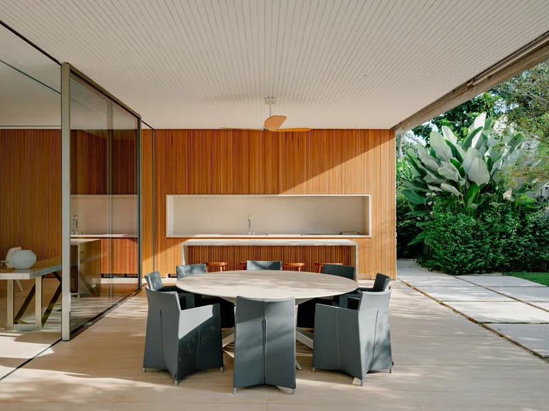 Covered dining terrace with slatted timber wall, limestone floor, and glass sliding doors opening to garden