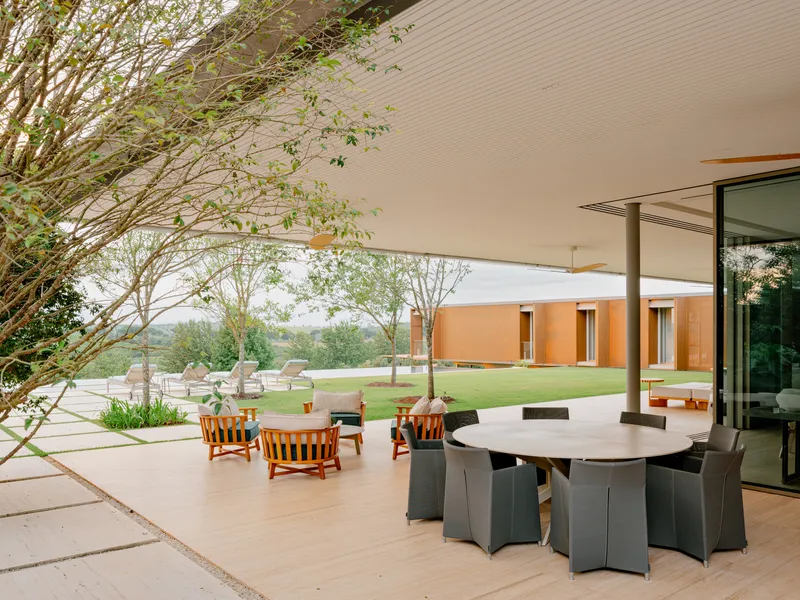 Covered terrace with dining table and lounge seating overlooking lawn and orange volume beyond