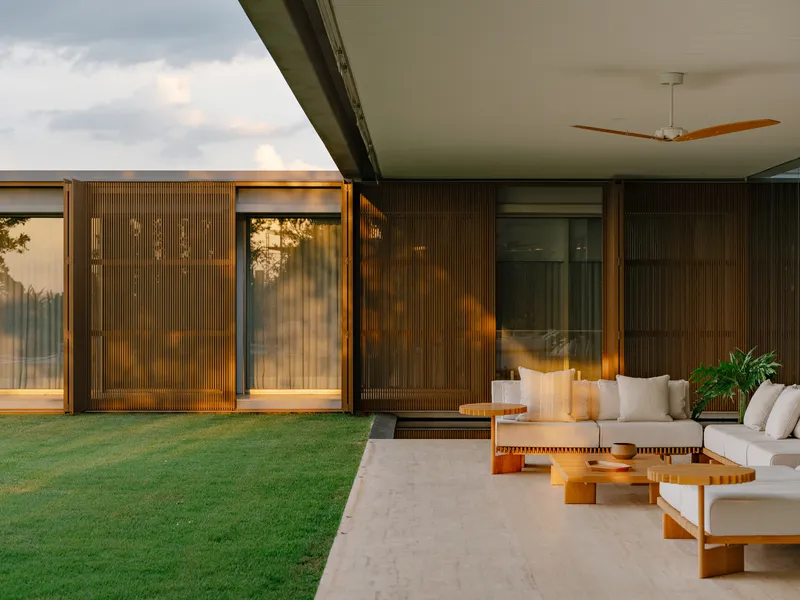 Facade with sliding corrugated screens and glass doors opening to furnished terrace at dusk