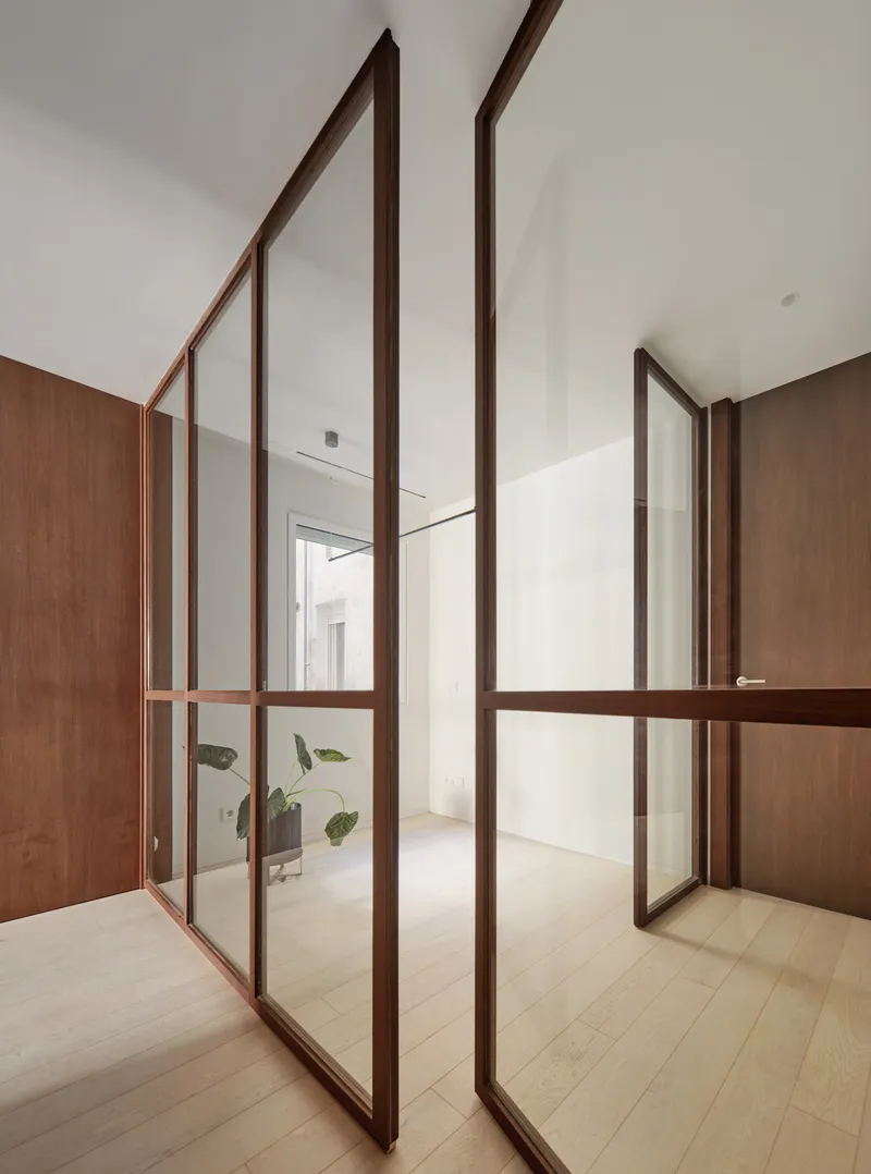 Glazed partition with slender timber frame separating rooms with pale wood flooring throughout