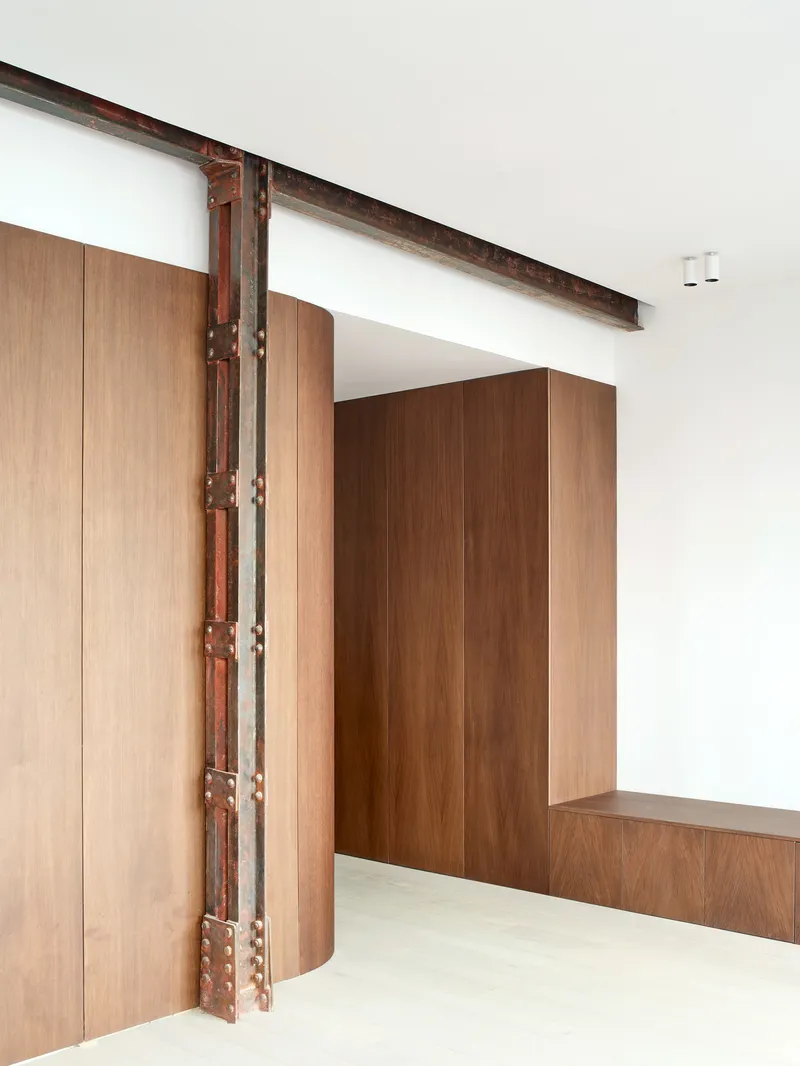 Detail of exposed steel column with rivets beside curved timber millwork and white walls