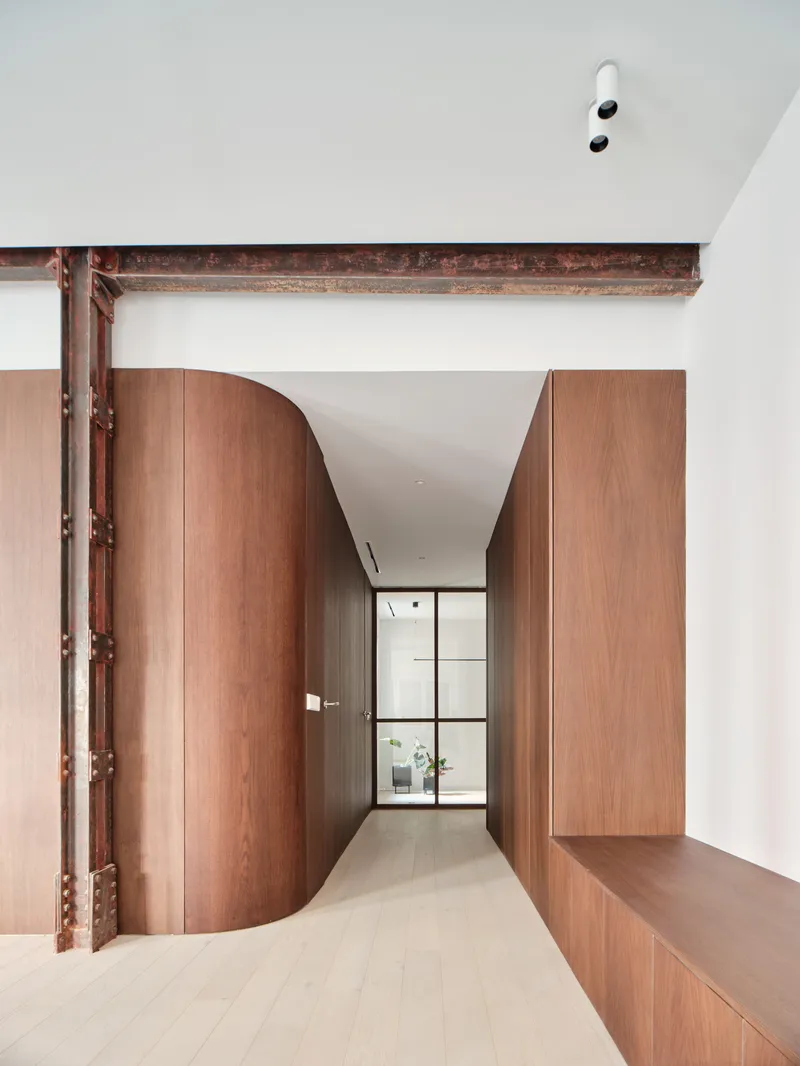 Corridor with curved wood cabinetry flanking an exposed rust-red steel beam under a white ceiling