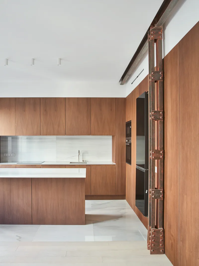 Kitchen island with white stone countertop framed by riveted steel columns and wood cabinetry