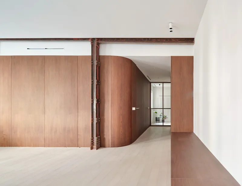 Corridor with curved timber door and exposed steel column alongside pale wood flooring