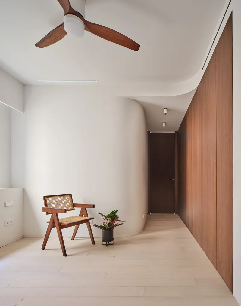 Bedroom with curved white wall leading to a corridor and wooden ceiling fan overhead