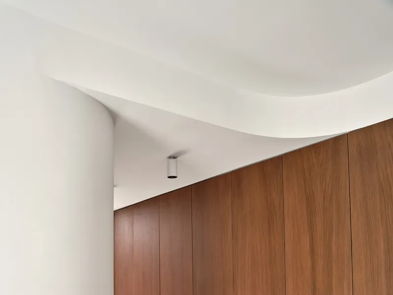 Detail of the curved white ceiling meeting a vertical walnut-paneled wall with recessed lighting