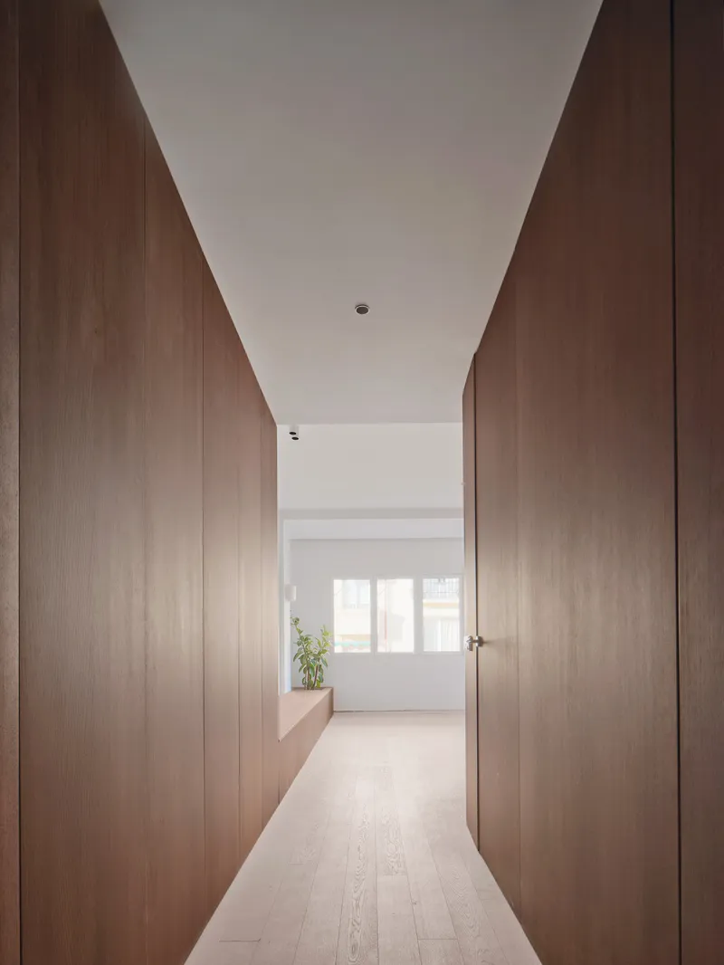 Hallway with walnut-clad walls and pale oak flooring leading to a sunlit room ahead